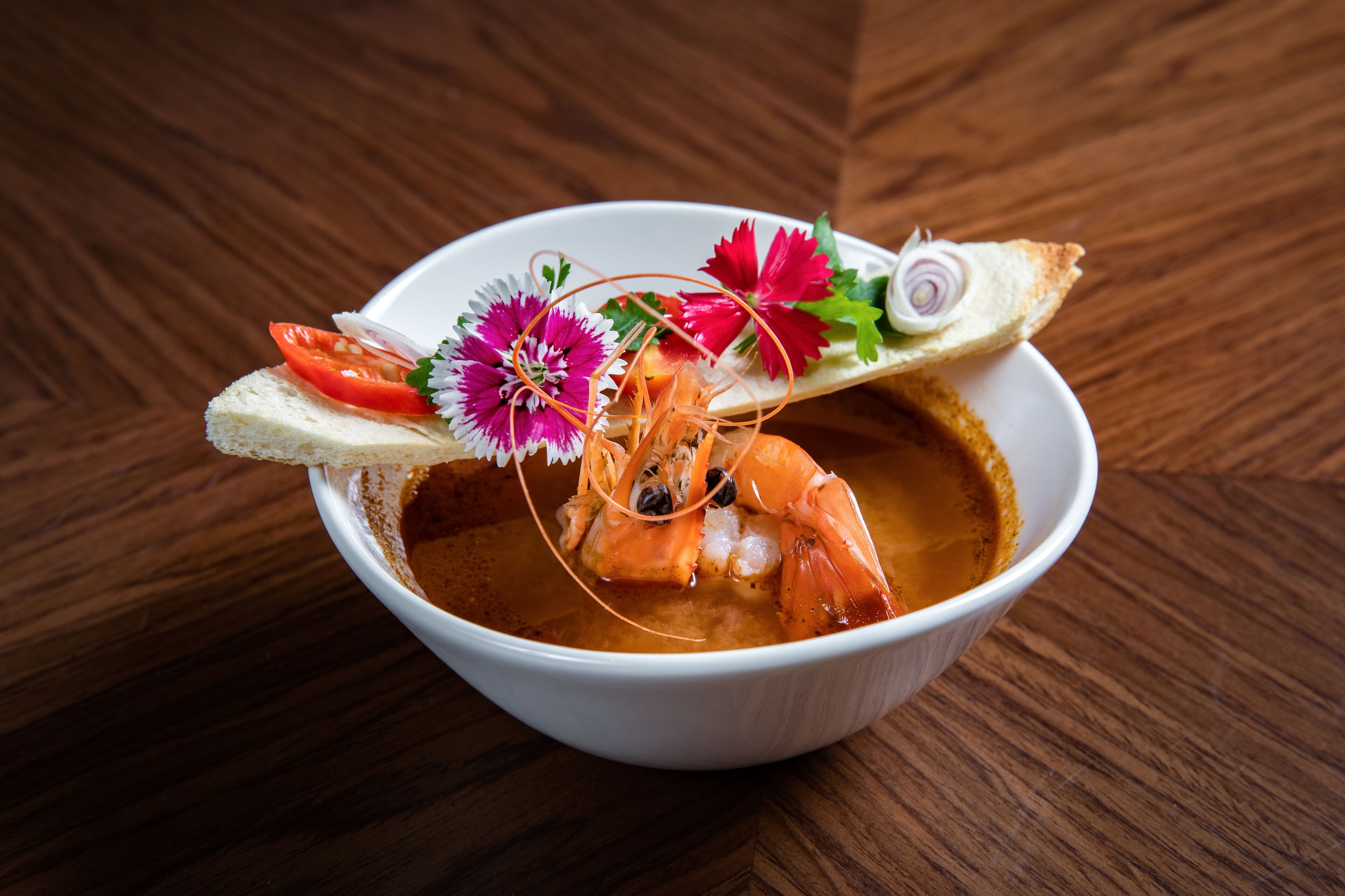A bowl of soup with shrimp, garnished with vegetables and flowers.