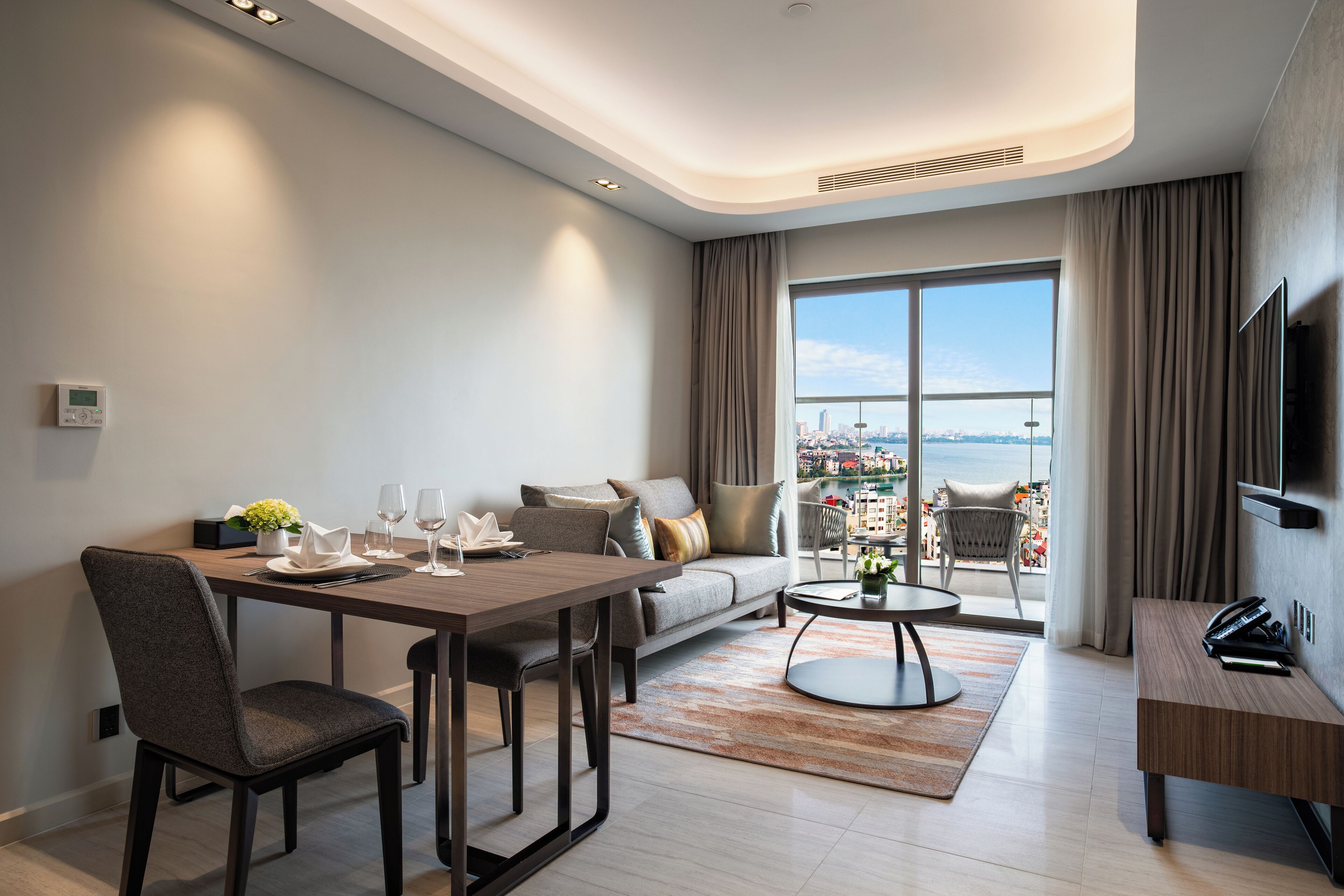 Ein modernes Wohnzimmer mit Essbereich, einer Couch, einem Balkon mit Stadtblick und einem an der Wand befestigten Fernseher.