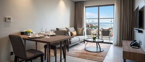 Ein modernes Wohnzimmer mit Essbereich, einer Couch, einem Balkon mit Stadtblick und einem an der Wand befestigten Fernseher.