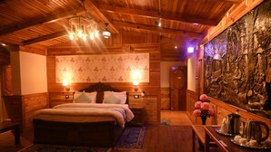 Habitación con decoración de madera, una cama grande, un banco de madera, una mesa con hervidor y un detalle decorativo en la pared.