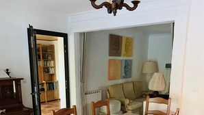 A dining area with a table covered in a protective sheet, surrounded by wooden chairs with green cushions. A chandelier hangs above the table, and a bookshelf is visible in the background. - Private pool in Mediterranean house on the French Riviera (Roquebrune-sur-Argens)