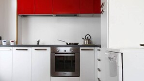 Una cucina con mobili bianchi, un forno in acciaio inossidabile e un pensile rosso.