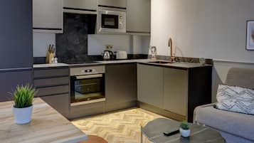 Una cocina compacta con electrodomésticos modernos, un comedor con una mesa y sillas de madera, y un sofá con un cojín estampado.