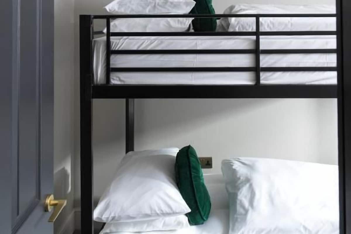 A bunk bed room with white bedding and a green pillow.