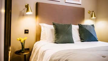 A neatly made bed with white and green pillows, a vase of yellow flowers, and two bedside lamps on a small table beside the bed.