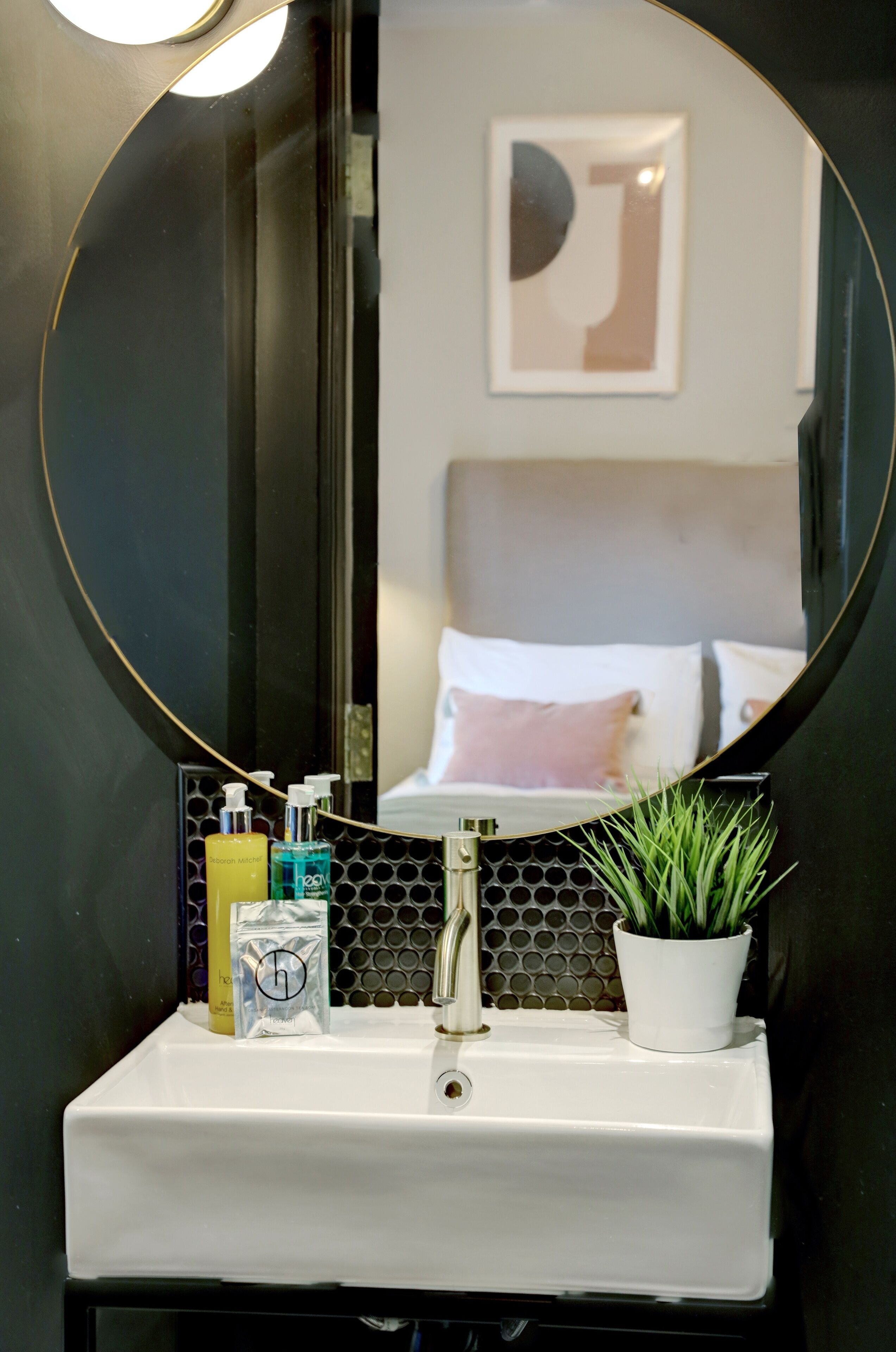 A bathroom with a round mirror, white sink, and toiletries.