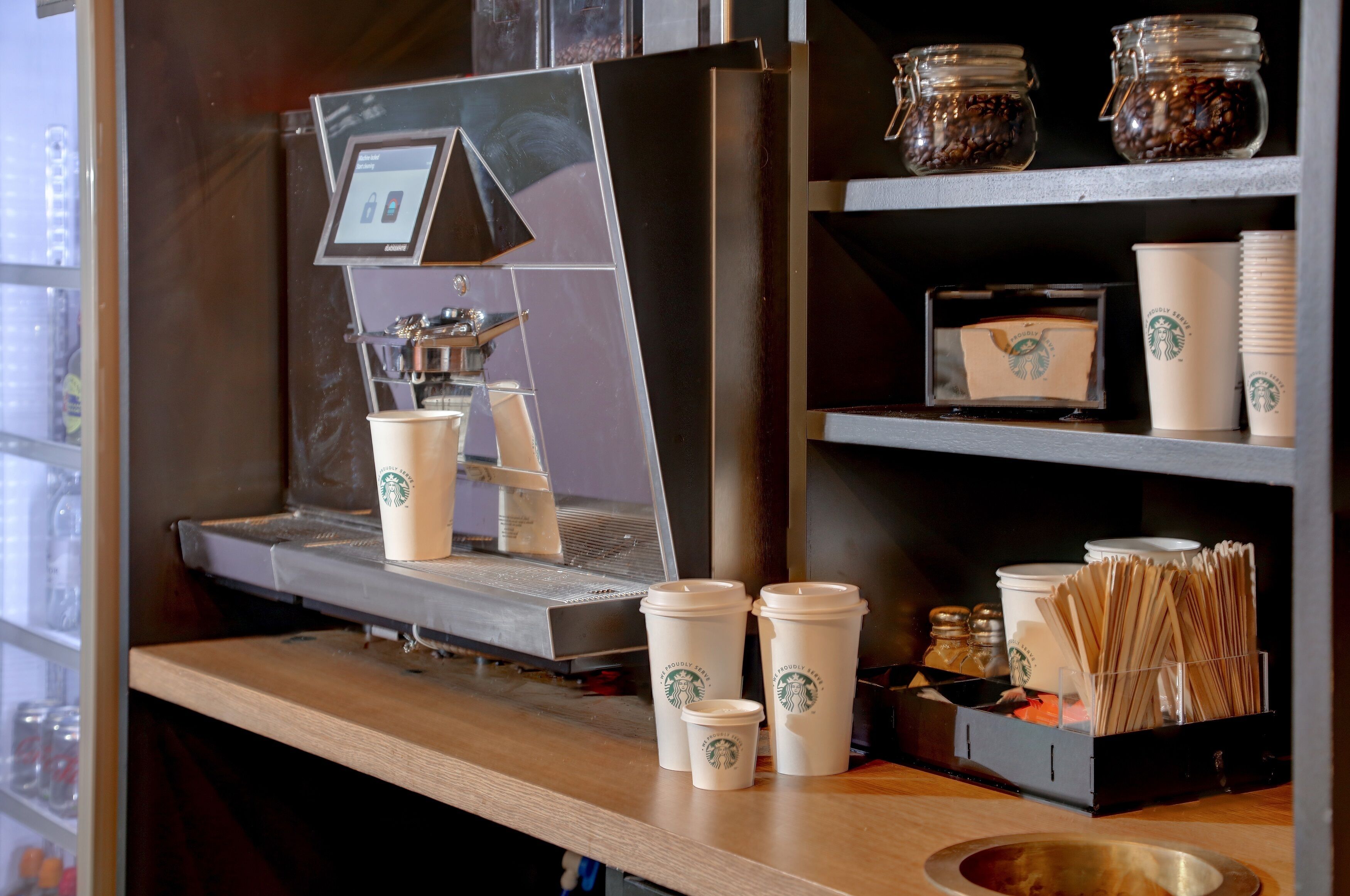 A coffee shop counter with a coffee machine, Starbucks cups, and a display of coffee beans.