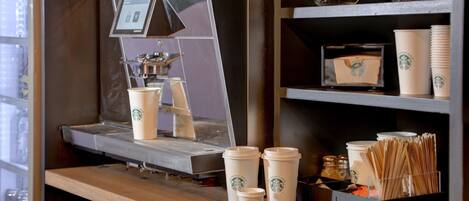 A coffee shop counter with a coffee machine, Starbucks cups, and a display of coffee beans.