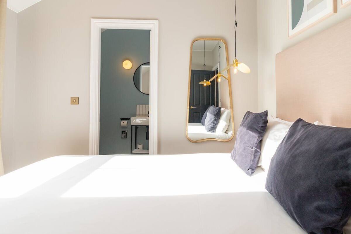 A hotel room with a large bed, a mirror, a bedside lamp, and a view of the bathroom.