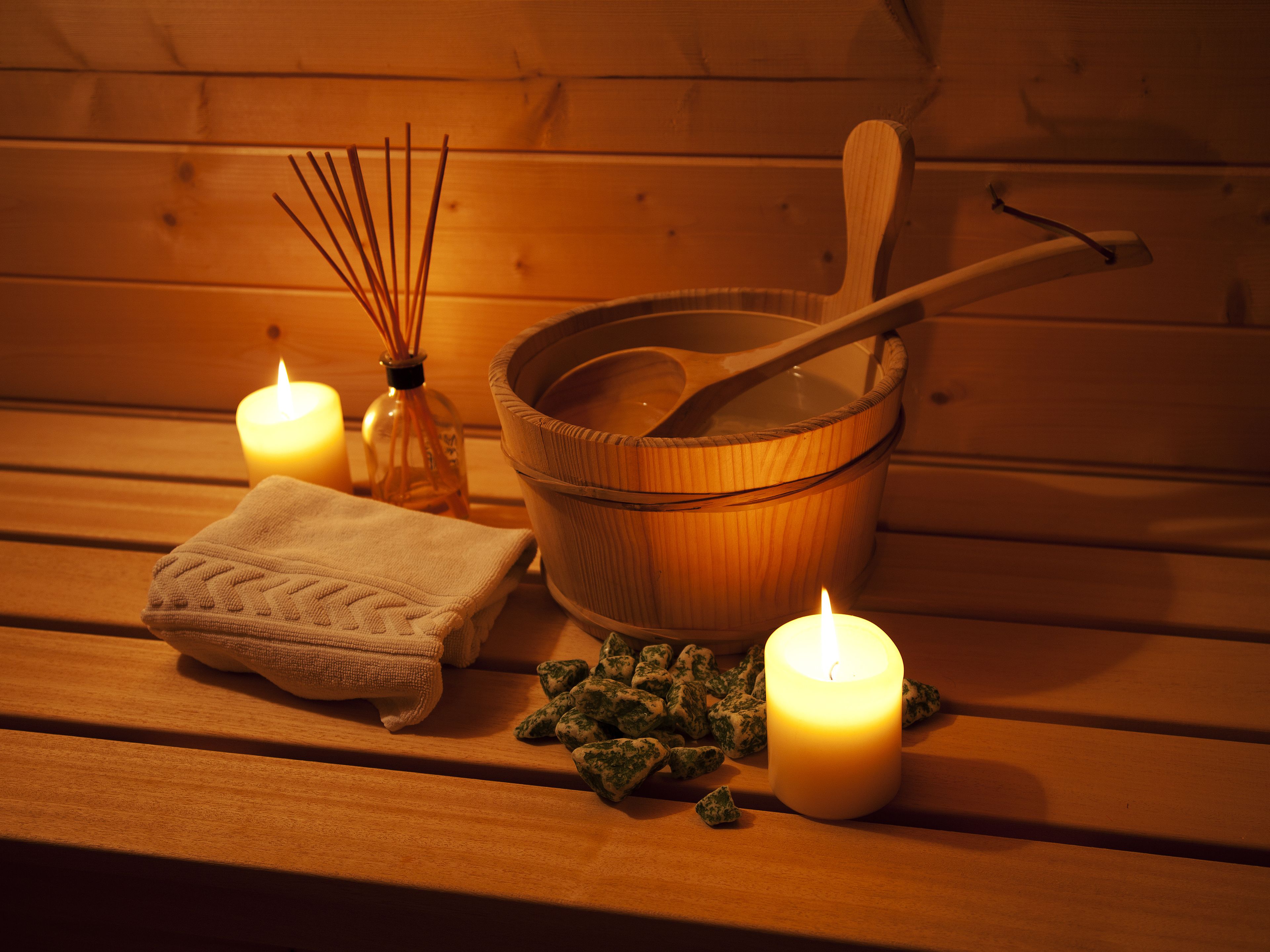 A wooden bench with a candle, a wooden bucket, a wooden spoon, and a bottle of reed diffuser.