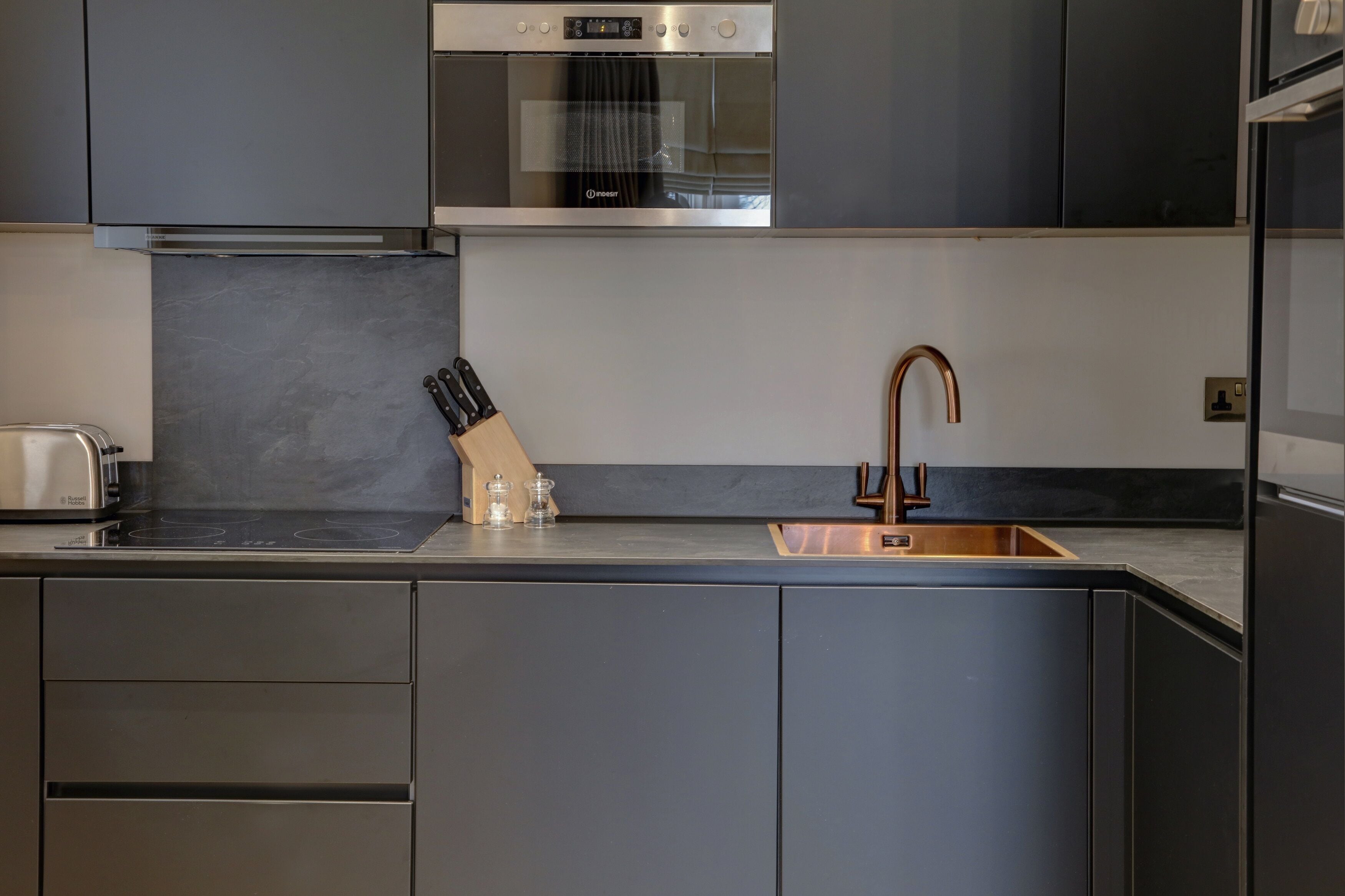 Eine moderne Küche mit dunklen Schränken, einem Edelstahlbackofen, einem Kupferarmaturen und einem Messerblock.