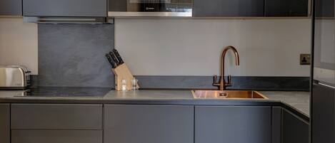 A modern kitchen with dark cabinetry, a stainless steel oven, a copper faucet, and a knife block.