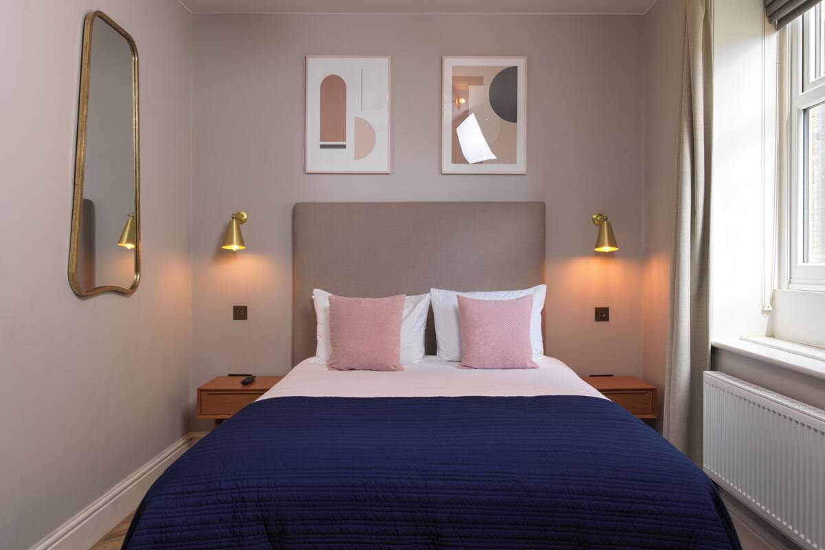 A bedroom with a large bed, two bedside tables, a mirror, and two wall-mounted lamps.