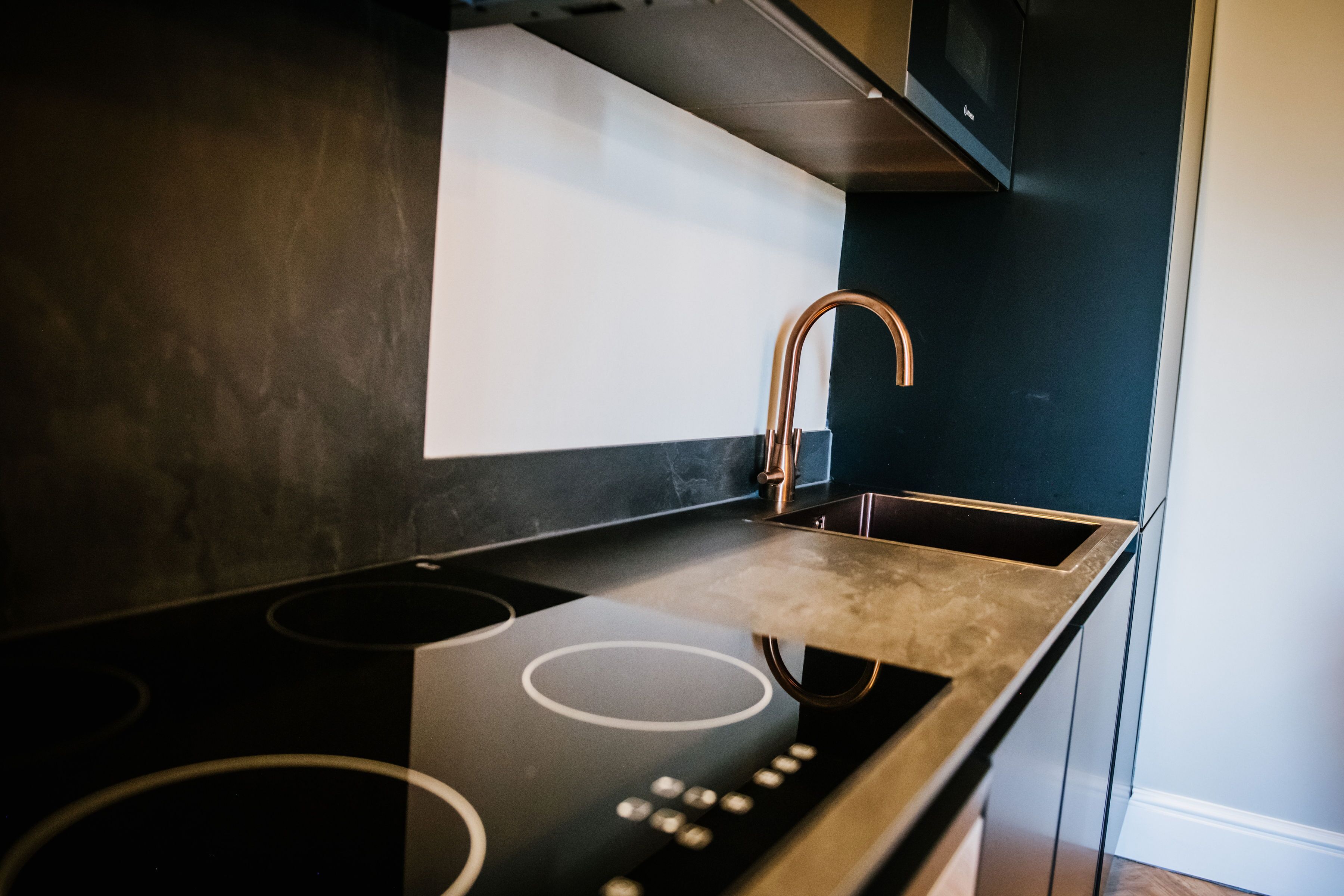 A modern kitchen with a black countertop, stainless steel sink, and a copper faucet.