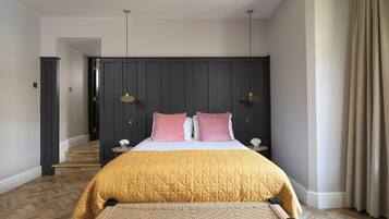 A bedroom with a large bed, a bench, a dark headboard, two bedside lamps, and a staircase in the background.