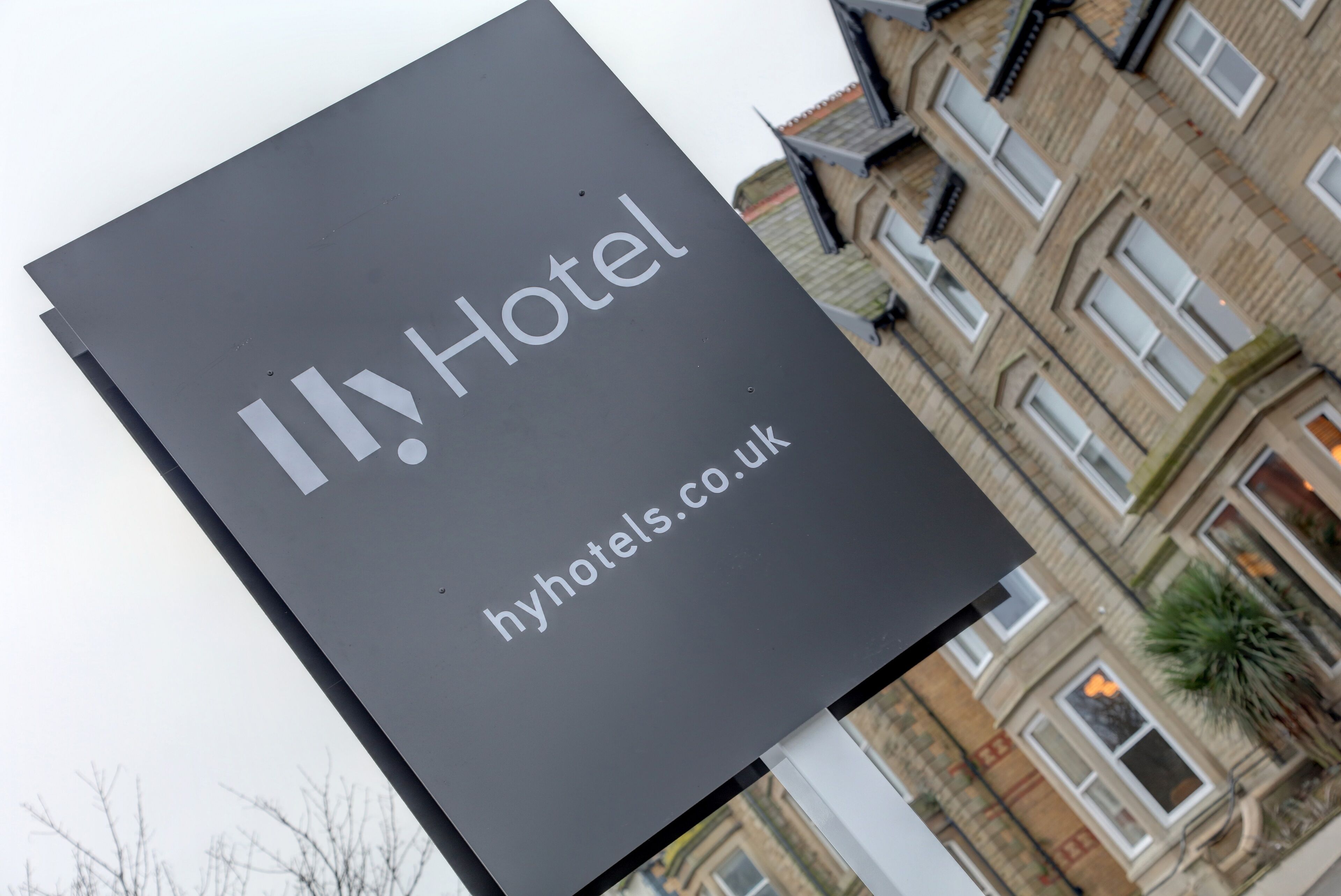 A sign for a hotel with the name "HyHotels.co.uk" and a view of a building with multiple windows and balconies.