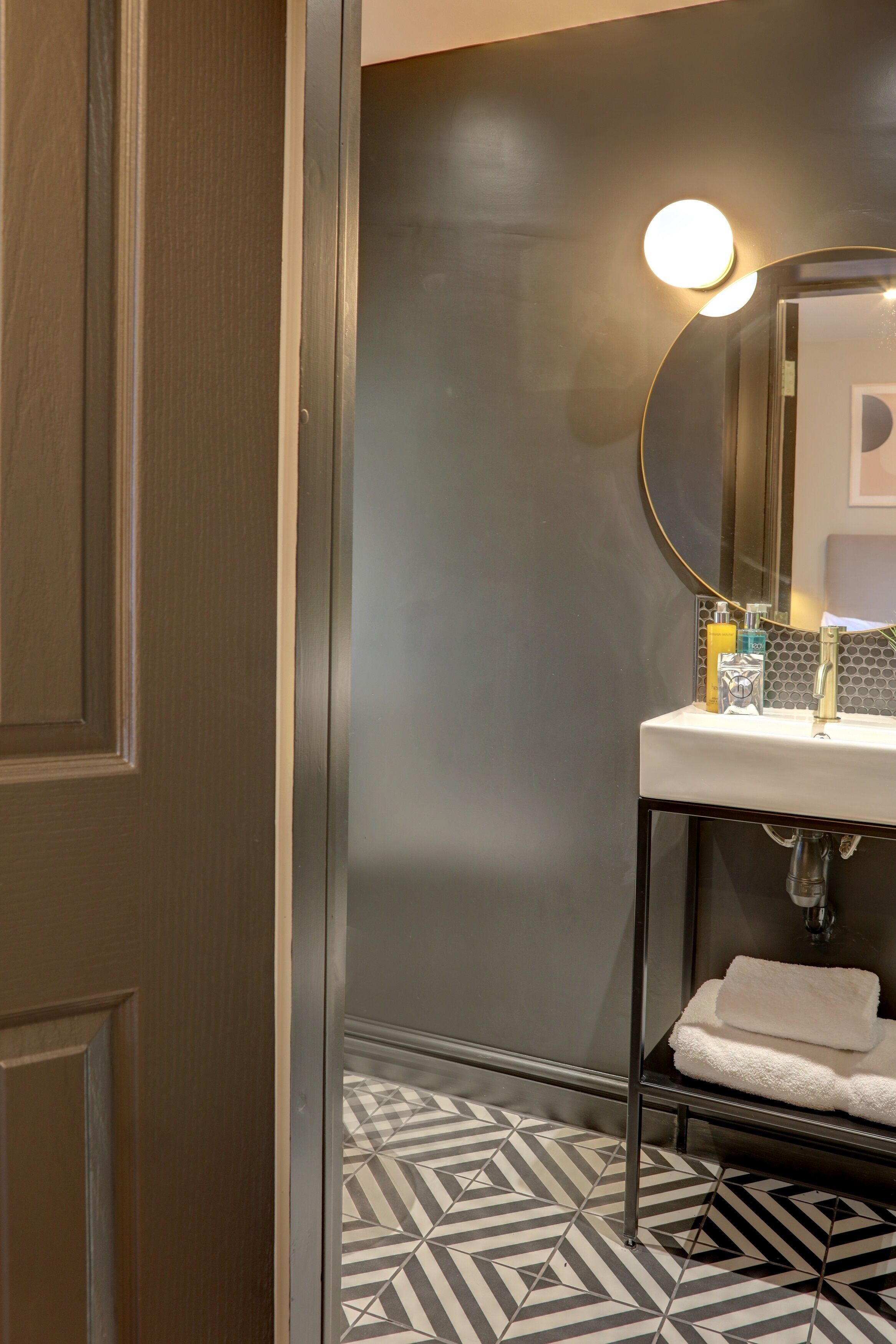 A bathroom with a round mirror, a white sink, and a towel rack.