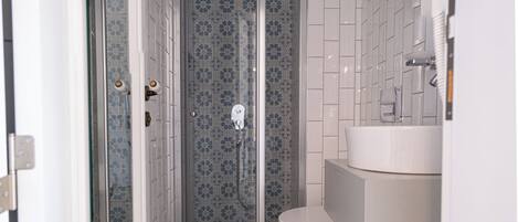 Un baño con ducha envuelta en vidrio, inodoro y lavamanos blancos, y un espejo.