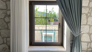 Una ventana con vista a un muro de piedra y una mesa con sillas afuera.