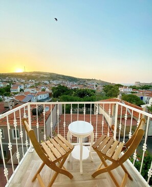 Un balcón con una mesa y dos sillas de madera, con vista a un pueblo de tejados rojos y cielo despejado.