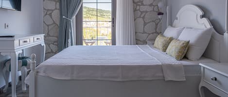 A bedroom with a stone wall, a bed with white bedding, a nightstand, a desk with a chair, and a window with curtains.