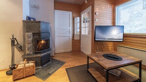 Una habitación acogedora con chimenea de piedra, televisor de pantalla plana, paredes de madera y una puerta que da a otra habitación.