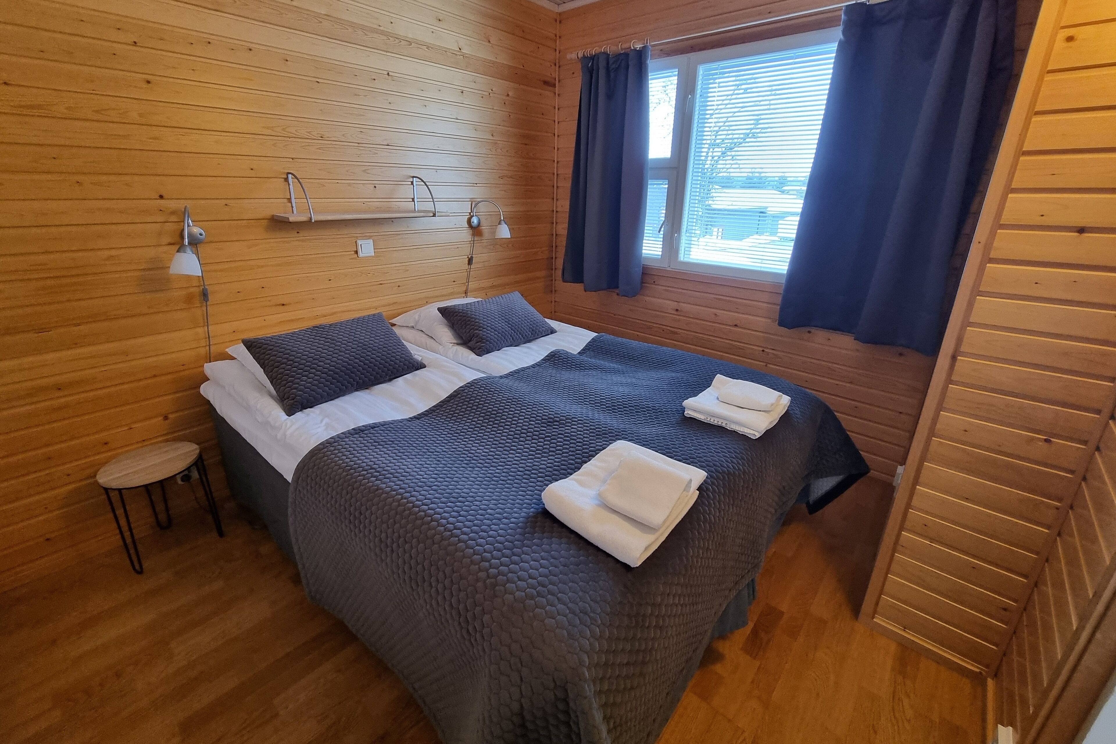 A wooden-paneled room with a bed, two bedside tables, and a window with curtains.