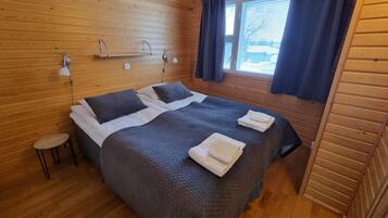 A wooden-paneled room with a bed, two bedside tables, and a window with curtains.