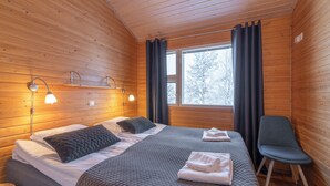 Habitación de cabaña de madera con una cama, dos lámparas de noche, una silla y una ventana con cortinas.