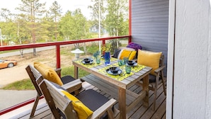 Una terraza de madera con una mesa dispuesta para dos, con mantel amarillo y cristalería azul.