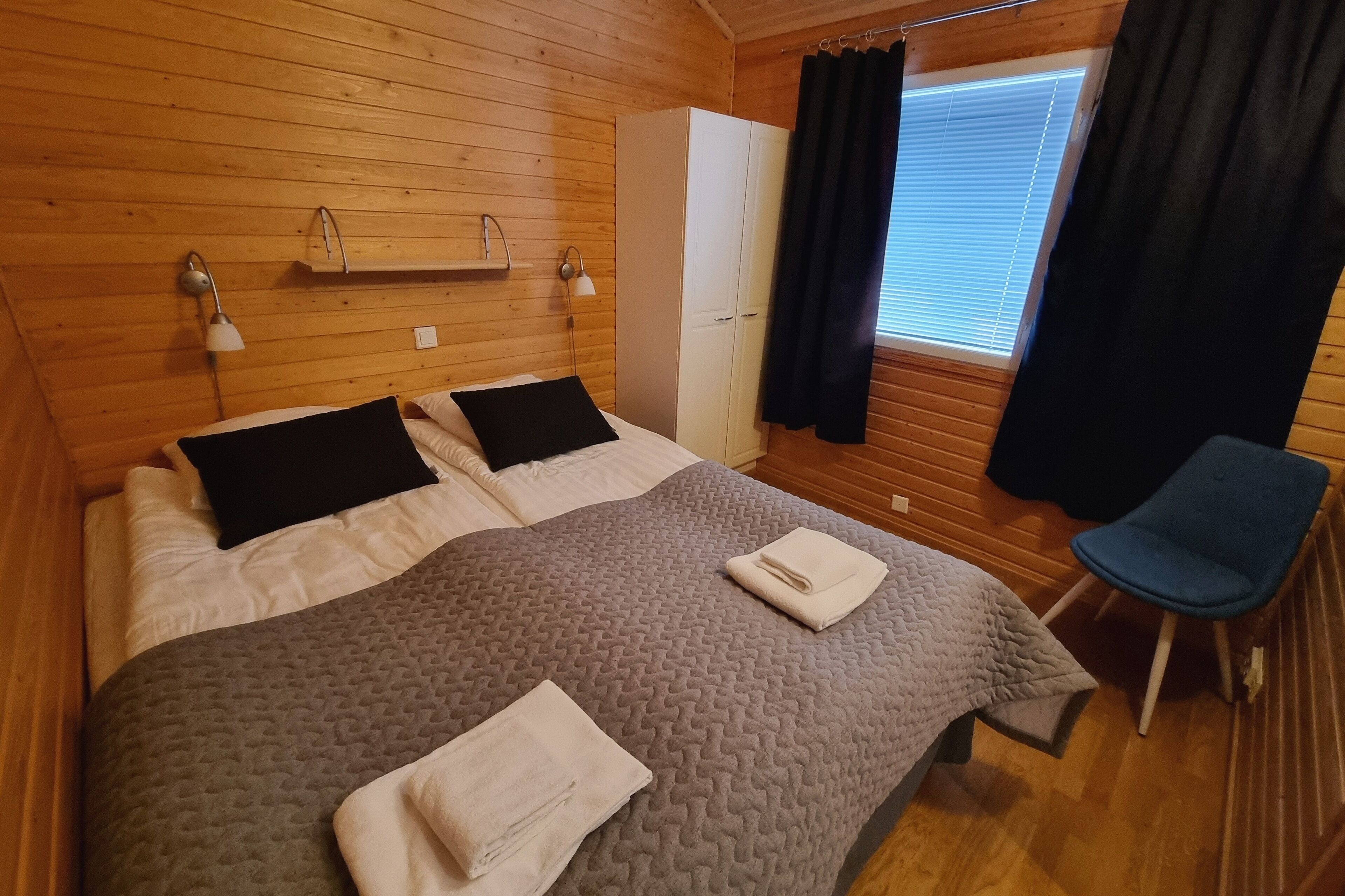 Um quarto aconchegante com cama, duas mesas de cabeceira com abajures, guarda-roupa e janela com cortinas.