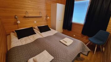 Um quarto aconchegante com cama, duas mesas de cabeceira com abajures, guarda-roupa e janela com cortinas.