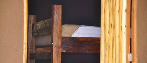 A wooden bed frame with a mattress inside a room with a dark wall and a wooden door.