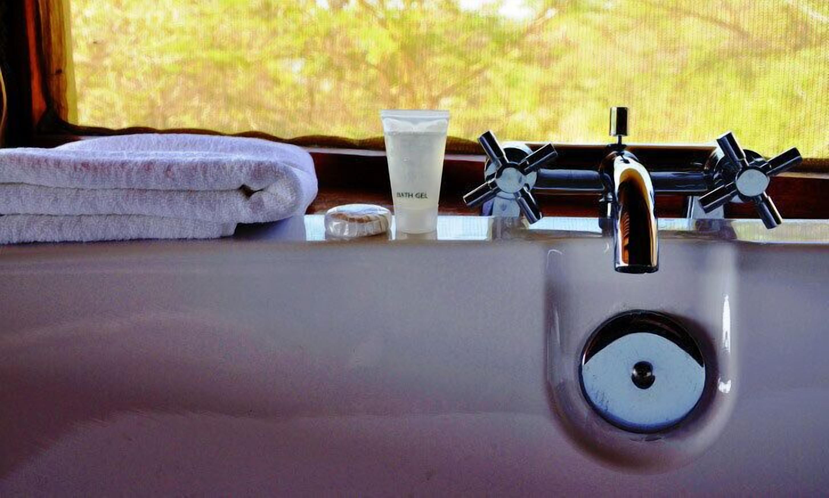 A bathroom sink with a towel, a bottle of bath gel, and a glass of water.