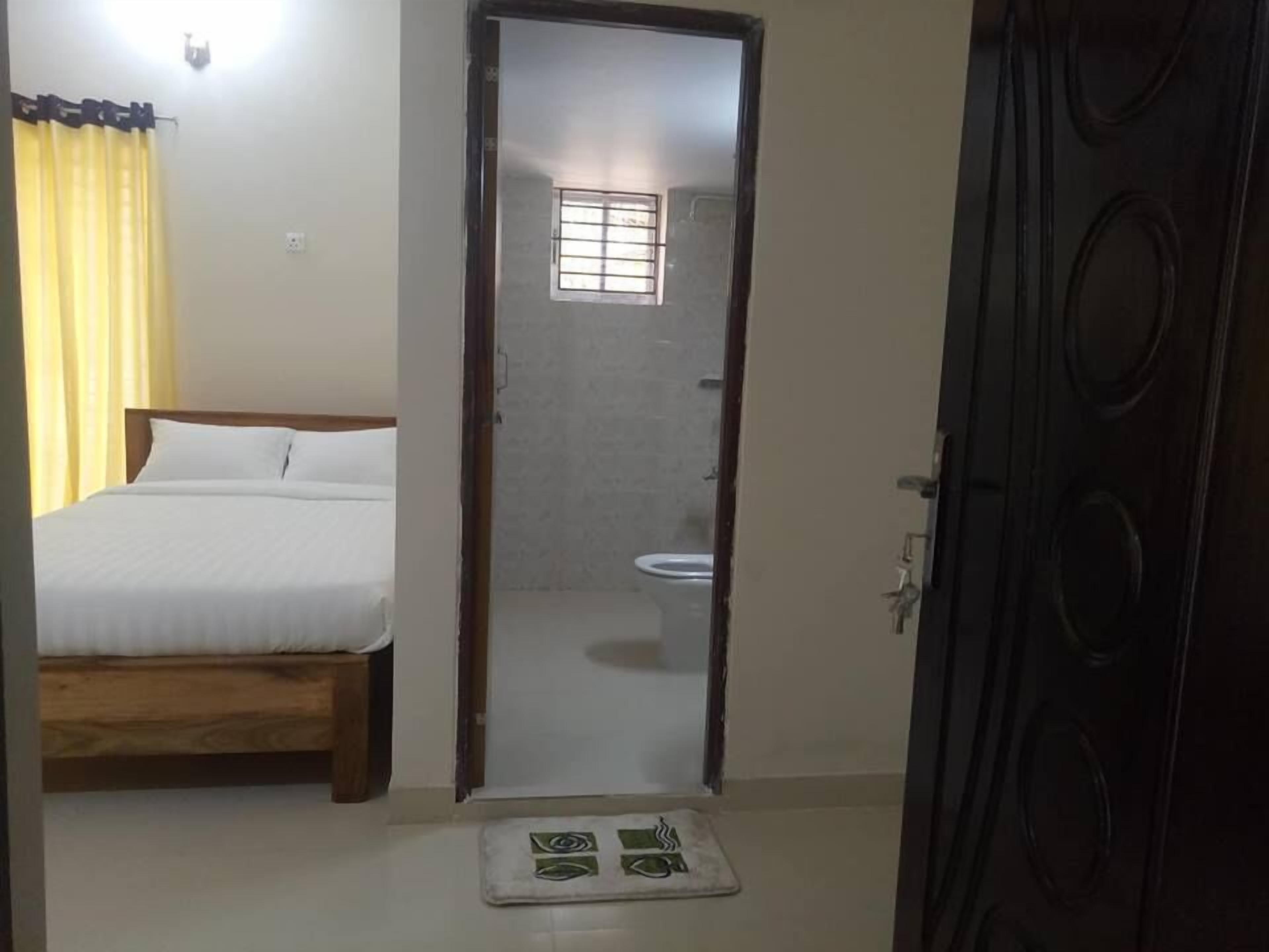 A bedroom with a bed, a bedside table, a bathroom with a toilet and a window, and a door.
