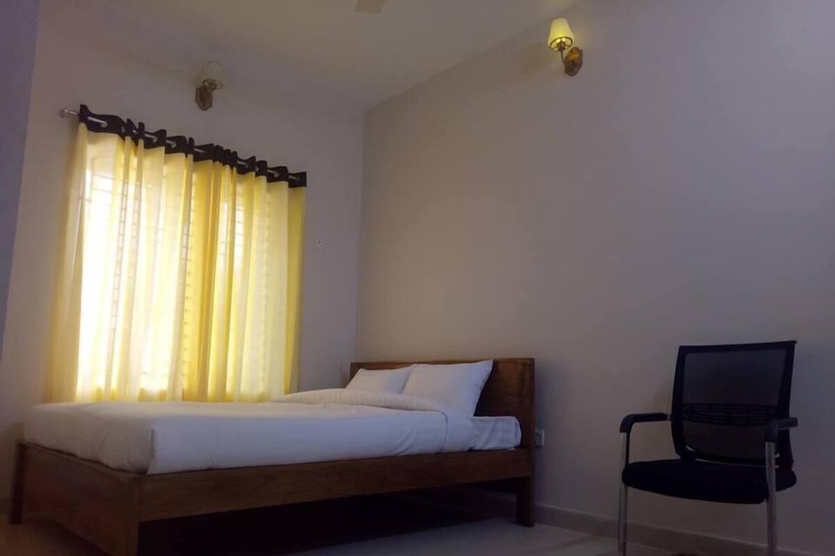 A bedroom with a wooden bed, a chair, and a window with yellow curtains.
