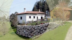 Un edificio blanco con techo rojo, un muro de piedra en primer plano y árboles al fondo.