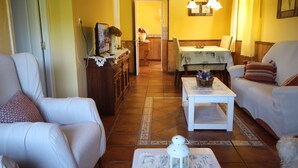 Una sala de estar con sofá, sillón y una mesa de centro. En el fondo, se ve una mesa de comedor con sillas.