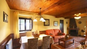 Una sala de estar acogedora con techo de madera, chimenea, sofá y comedor con mesa y sillas.
