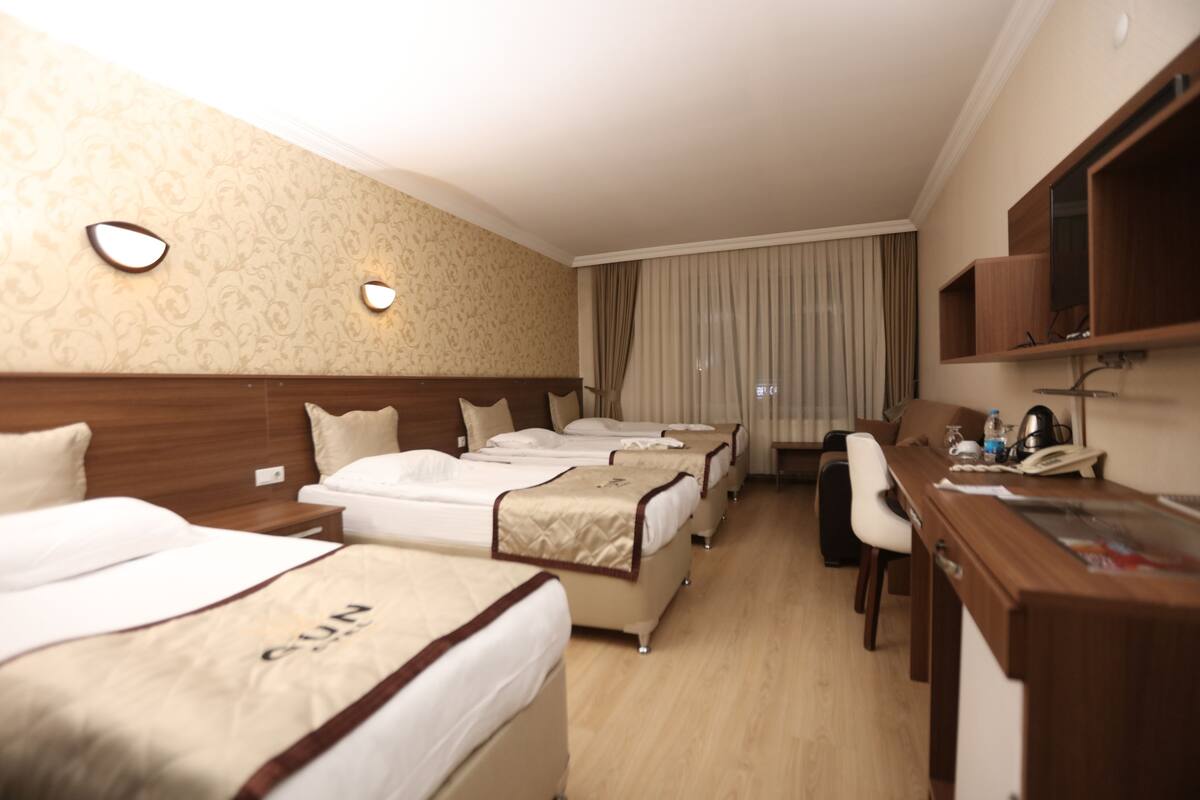 Ein Hotelzimmer mit drei Betten, einem Schreibtisch und einem Fernseher.
