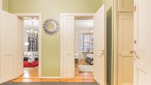 A hallway with open doors leading to a living room with a chandelier, a mirror, and a red rug. - Go Happy Home Apartment Mikonkatu 18 2 (Helsinki)