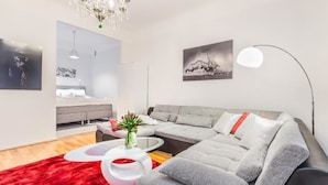 A modern living room with a grey sectional sofa, a red rug, a white coffee table, and a chandelier. - Go Happy Home Apartment Mikonkatu 18 2 (Helsinki)