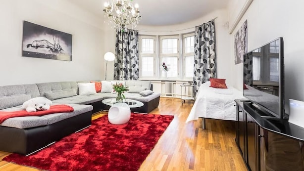 A modern living room with a grey sectional sofa, a red rug, a white coffee table, and a TV on a black stand. - Go Happy Home Apartment Mikonkatu 18 2 (Helsinki)