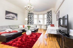A modern living room with a grey sectional sofa, a red rug, a white coffee table, and a TV on a black stand. - Go Happy Home Apartment Mikonkatu 18 2 (Helsinki)