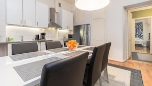 A modern kitchen with white cabinets, a stainless steel refrigerator, and a dining area with a table set for two. - Go Happy Home Apartment Mikonkatu 18 2 (Helsinki)