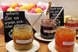 Une table avec des pots de confiture, un panier d’œufs de couleurs vives et des panneaux avec du texte en allemand.