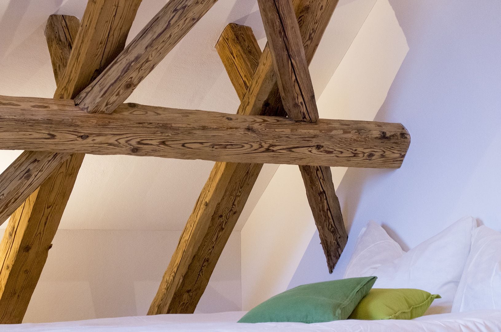 Ein Zimmer mit freiliegenden Holzbalken und einem Bett mit weißen und grünen Kissen.