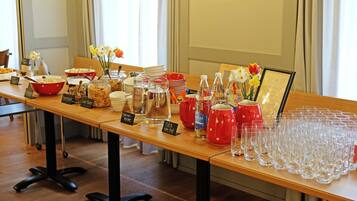 A buffet table with various food items and drink dispensers, arranged on a wooden table with a glassware set at the end.