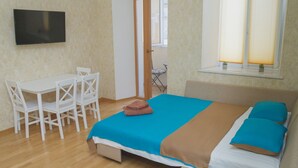 Habitación con cama, escritorio y silla. Hay un televisor en la pared y una ventana con persianas.