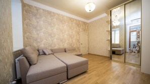 Una habitación amplia con un sofá grande, suelo de madera y una puerta corredera de cristal que da a otra habitación.